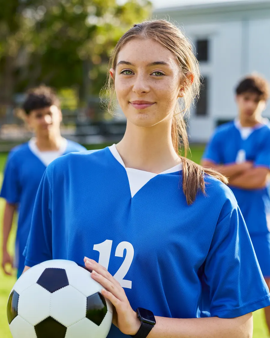 Spielerin mit der Rueckennummer 12 haelt einen Ball im Arm,
                  im Hintergrund warten vier Mitspieler auf dem Rasen.